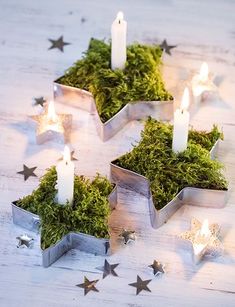 three candles are placed in small metal containers with moss and stars around them on a white wooden table