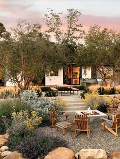 an outdoor dining area with wooden chairs and table surrounded by rocks, plants and trees