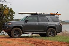 a vehicle with a surfboard on top is parked by the water