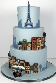 a three tiered blue cake with the eiffel tower in the background