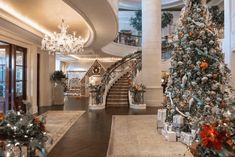 a large christmas tree in the middle of a room with stairs and chandeliers