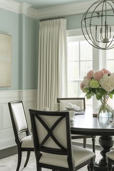 a dining room table and chairs with flowers in vase on the centerpiece, along with curtains