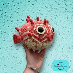 a hand holding a red and white knitted fish ornament on a blue background