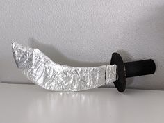 a knife that is wrapped in tinfoil on a white counter top with a black handle