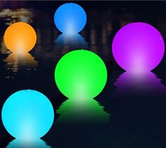 four different colored balls sitting on top of a black surface with water reflecting off the ground