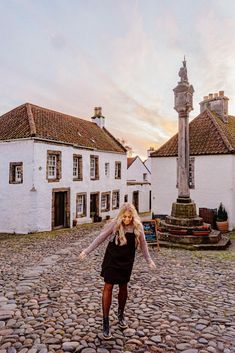 a woman standing in the middle of a cobblestone road with buildings behind her