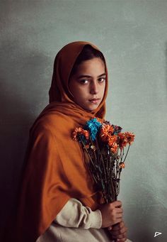 a woman wearing a shawl and holding flowers in her hands, looking at the camera