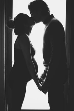 black and white photograph of a man kissing a woman's head in front of a window