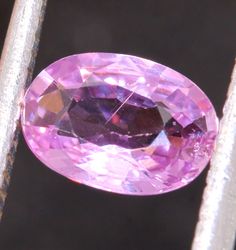 an oval shaped pink diamond sitting on top of a piece of silver metal fence post