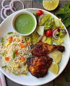 a white plate topped with chicken, rice and veggies next to a bowl of green sauce