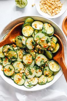 cucumber salad in a white bowl with wooden serving spoons on the side