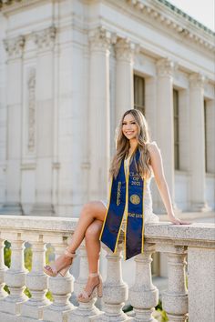 a beautiful young woman sitting on top of a stone wall next to a white building