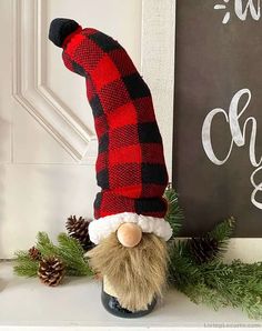 a red and black plaid gnome hat sitting on top of a white mantle next to pine cones