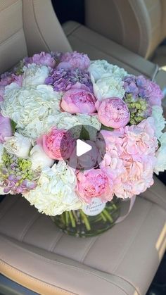 a vase filled with pink and white flowers on top of a car seat next to a steering wheel