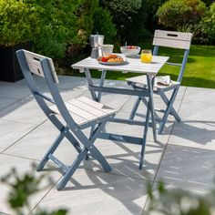 an outdoor table and two chairs with food on the table, in front of some bushes