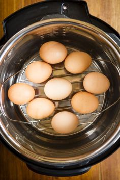 six brown eggs are in the bottom of an electric pressure cooker on a wooden table