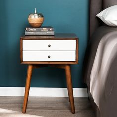 a nightstand with two books on top of it next to a bed and blue wall