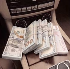 a bunch of money sitting on top of a car dashboard next to a cell phone