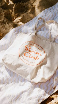 a white tote bag sitting on top of a towel next to the ocean shore