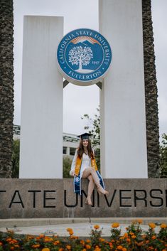 a woman sitting in front of the state university sign with flowers and trees around her