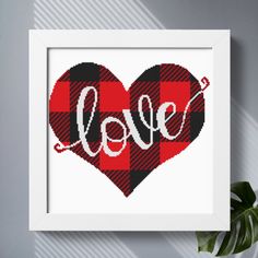 a red and black plaid heart with the word love on it in white frame next to a potted plant