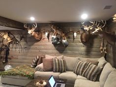 a living room filled with lots of deer heads mounted on the wall above a couch