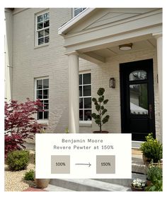 the front porch of a house with white columns and black doors, next to a red flowering bush