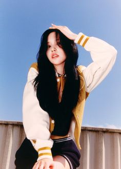 a woman with long black hair sitting on top of a metal wall holding her hand up to her head