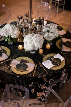 the table is set with white flowers and gold plates, candles, and napkins