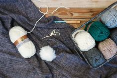 several balls of yarn sitting on top of a blanket next to scissors and knitting needles