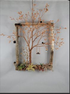 a wooden frame with an orange tree and birds hanging from it's branches in front of a gray wall