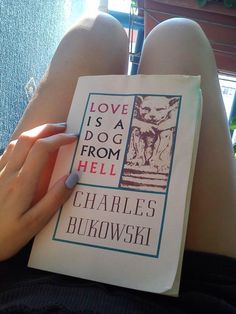 a person holding a book in their lap with the title love is a dog from hell written on it