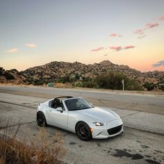 a white sports car is parked on the side of the road with mountains in the background