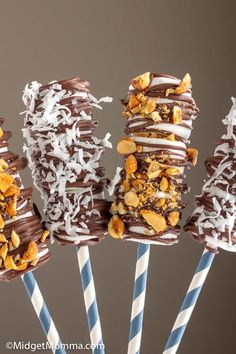 four chocolate covered donuts on top of blue and white striped straws with toppings