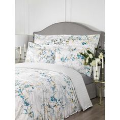 a white bed with blue and yellow flowers on the comforter is in front of a gray headboard