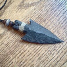 a wooden necklace with a black and silver pendant hanging from it's side on a wood table