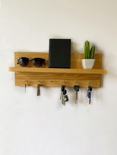 a wooden shelf with keys and sunglasses hanging on the wall next to a potted cactus