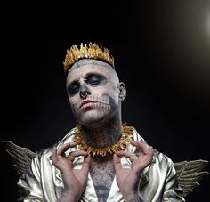 a man with his face painted like a skeleton wearing a crown and holding hands up to his chest