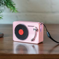 a pink radio sitting on top of a wooden table next to a phone and plant