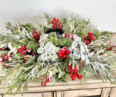 a christmas wreath with red berries and greenery on an old wooden table in front of a white wall