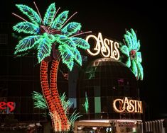 palm trees are lit up at night in front of the casino and casino sign on the building