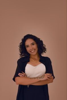 a woman with her arms crossed posing for a photo in front of a brown background