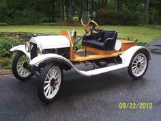 an old fashioned car is parked on the side of the road in front of some trees