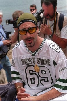 a man wearing sunglasses and a hat is sitting on a bench with other people around him