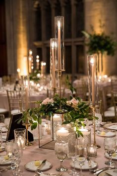 a table with candles and flowers in vases on it, surrounded by other place settings