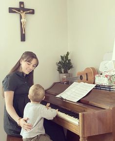 a woman playing the piano with her toddler in front of a crucifix