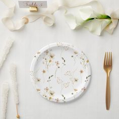 a white plate with flowers on it next to gold forks and napkins