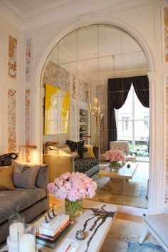 a living room filled with furniture and flowers on top of a coffee table in front of a mirror