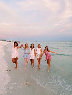 four girls are walking on the beach in front of the ocean with their arms around each other