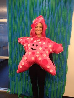 a woman in a pink starfish costume standing next to a green curtain with white polka dots